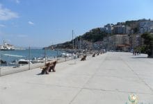 a concrete walkway with benches and boats on the water